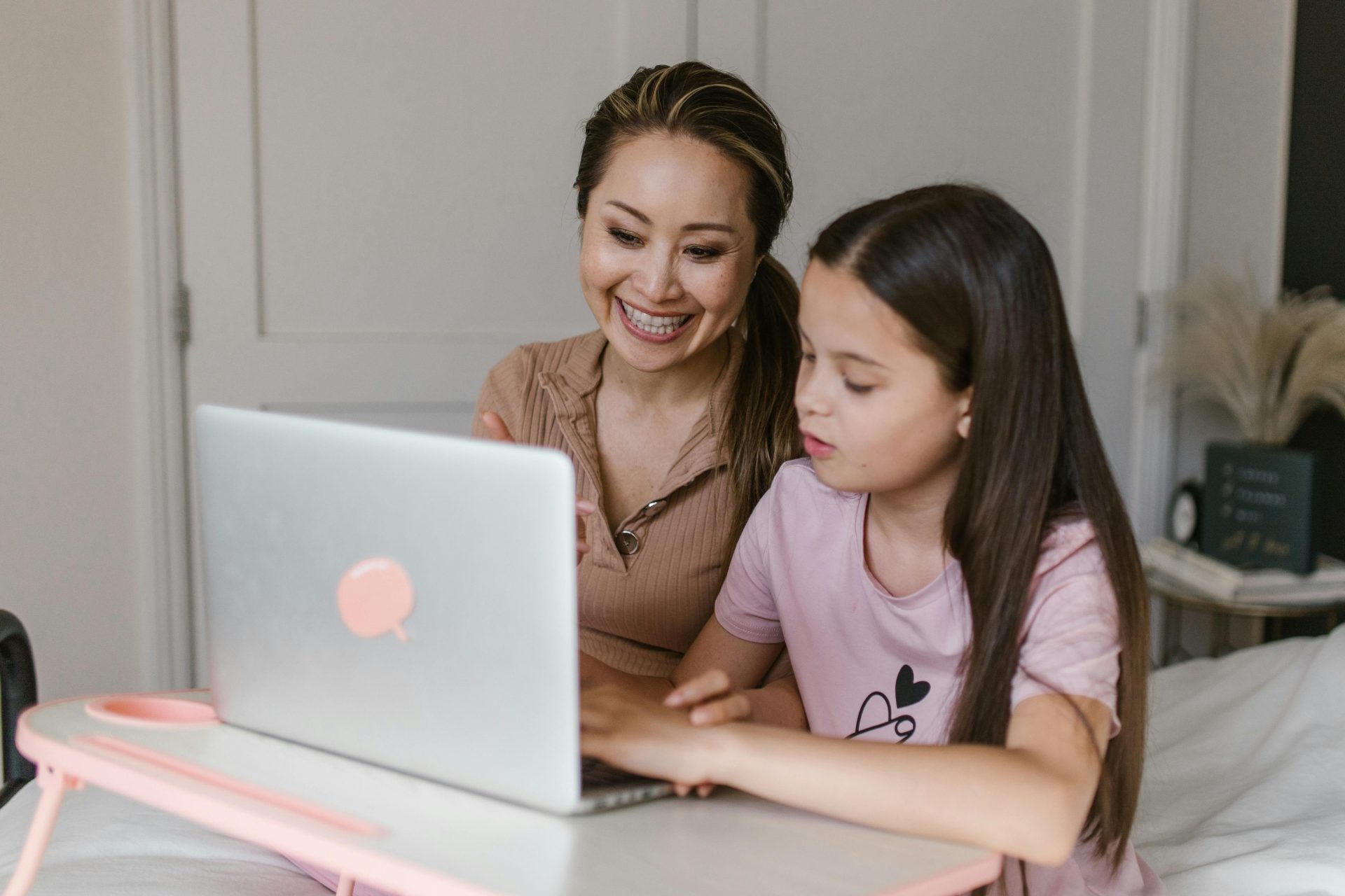 Mutter und Tochter lächeln und lernen gemeinsam zu Hause mit einem Laptop.